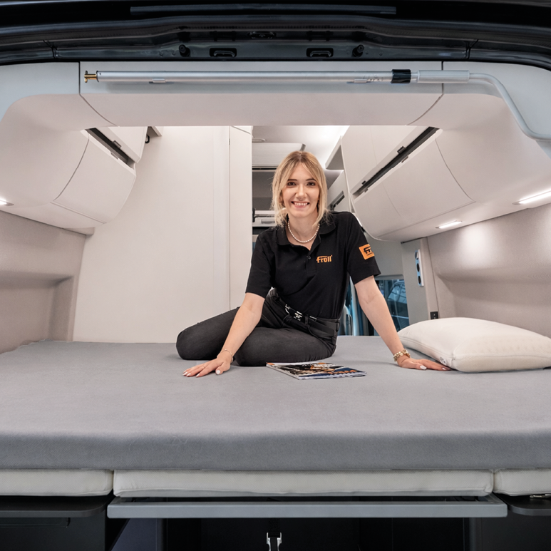 Person sitzt auf dem grauen Froli Spannbettlaken im Heckbett des VW Grand California 600