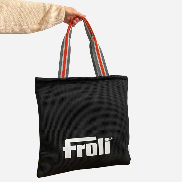 Hand trägt die schwarze Froli Tragetasche mit Logo und grauen Tragegriffen mit orangefarbenen Streifen
