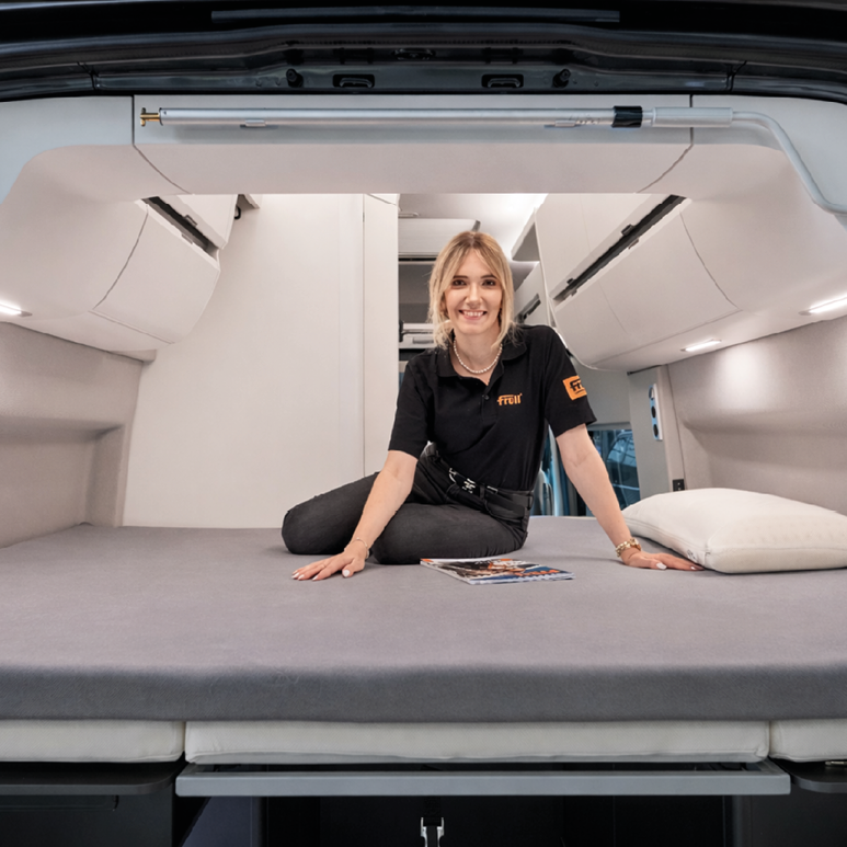 Person sitzt auf dem grauen Froli Spannbettlaken im Heckbett des VW Grand California 600